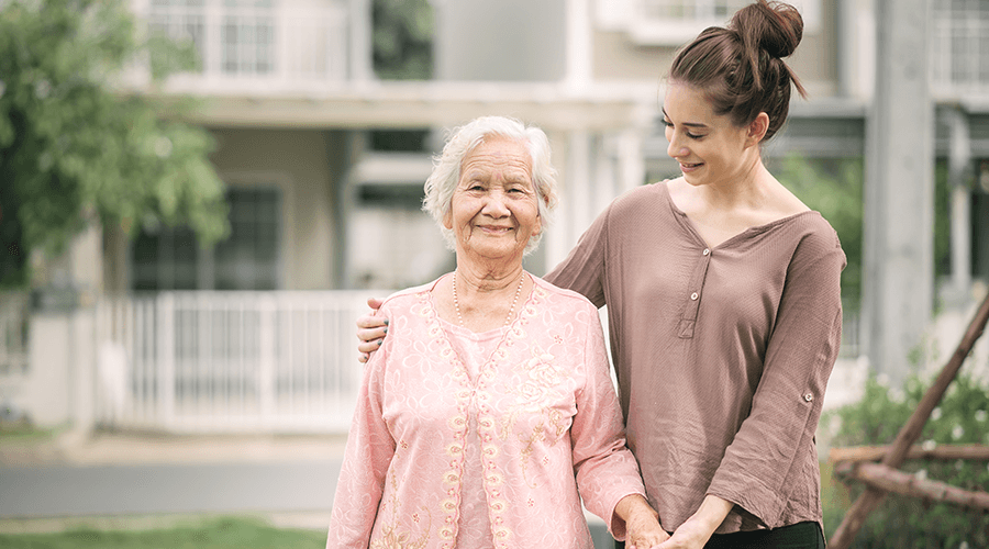 Caregiver and elderly woman walking outside on a nice day.