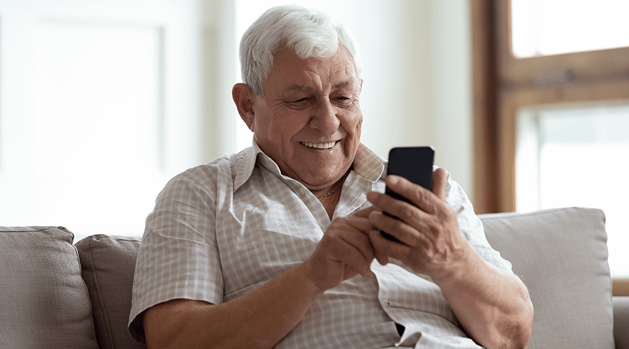 Senior gentleman sitting on a couch smiling as he uses his mobile phone.