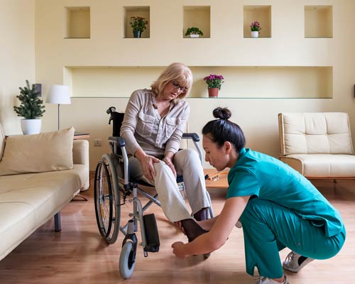 Nurse assisting a woman in a wheelchair with her shoes.