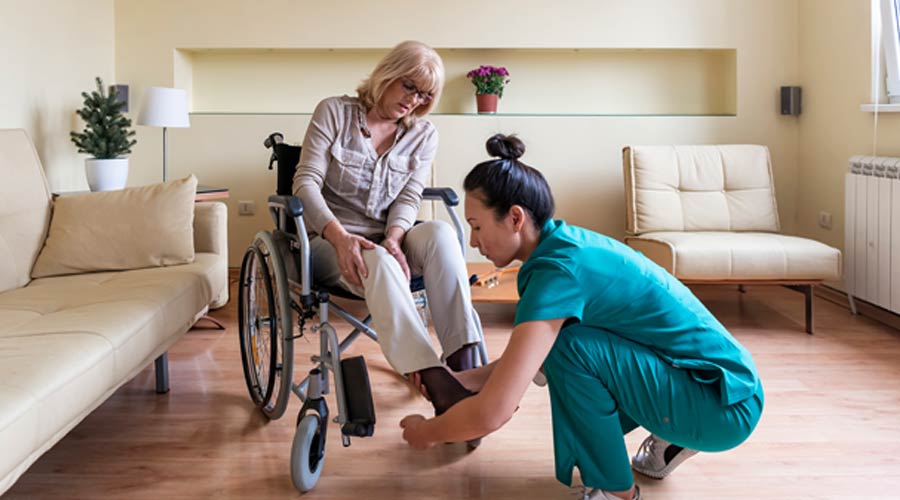 Nurse assisting a woman in a wheelchair with her shoes.