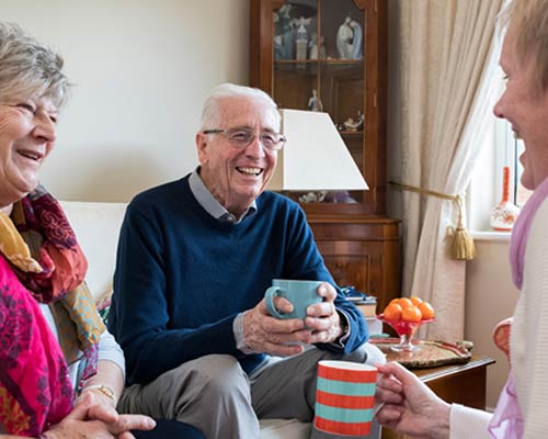 3 seniors laughing while drinking coffee in the living room.