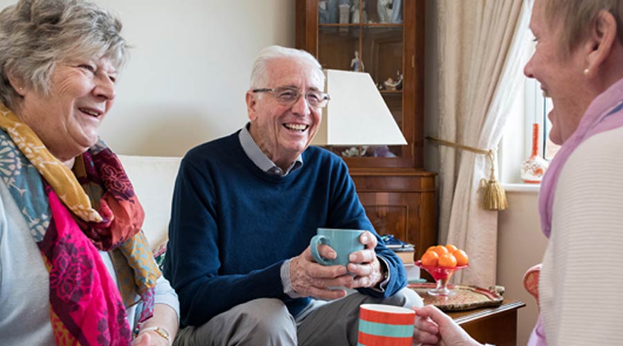 3 seniors laughing while drinking coffee in the living room.