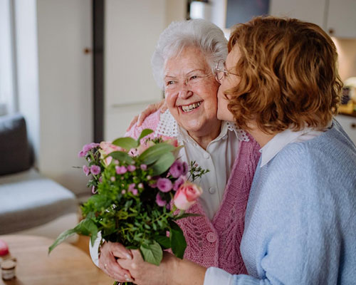 Daughter giving her mom flowers and kissing her on the cheek.