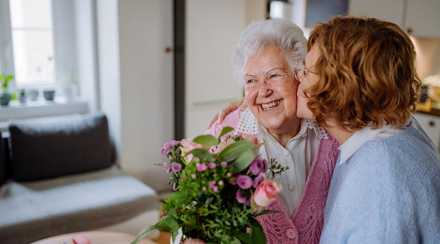 Daughter giving her mom flowers and kissing her on the cheek.