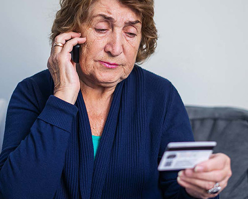 Woman looking disgusted while talking on the phone and holding her credit card.