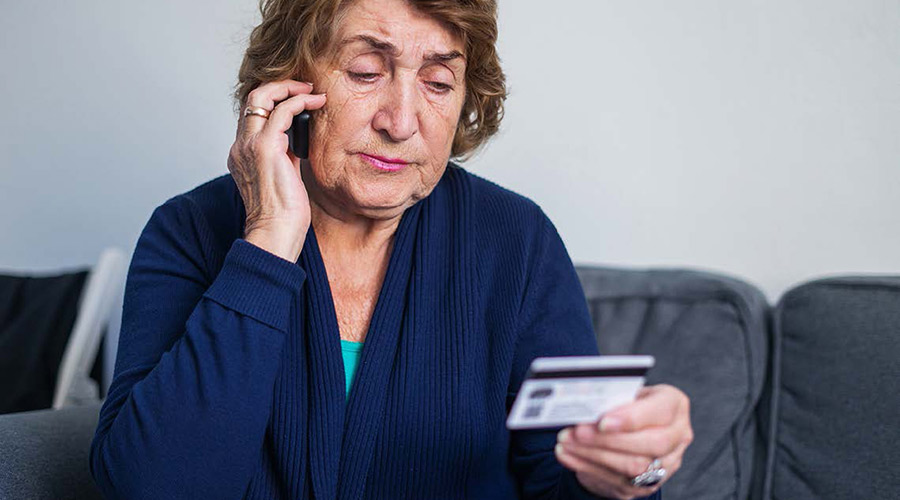 Woman looking disgusted while talking on the phone and holding her credit card.