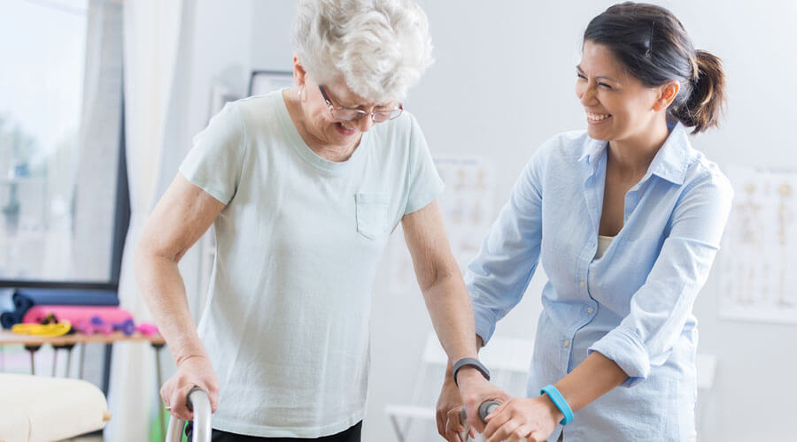 Woman helps another woman with her walker while smiling.