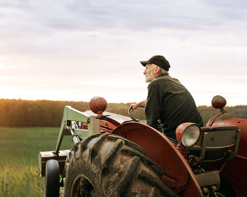 Man on a tractor in front of a sunset.