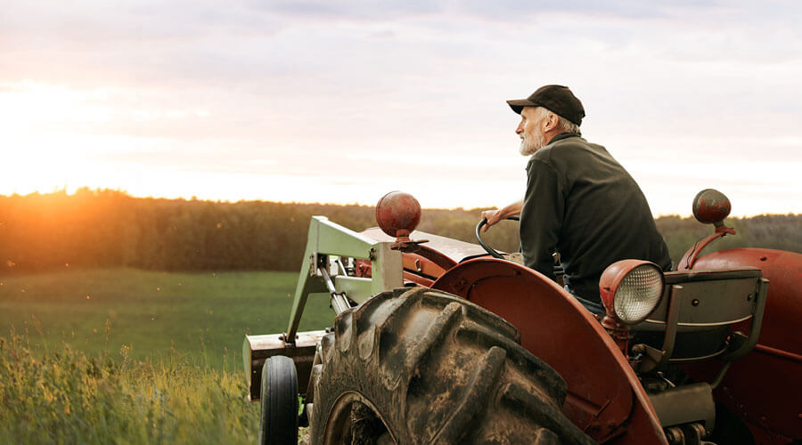 Man sitting on a tractor in front of a sunset.
