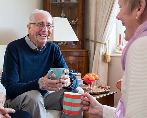 Senior adults enjoying each others company as they have tea in a sitting room.
