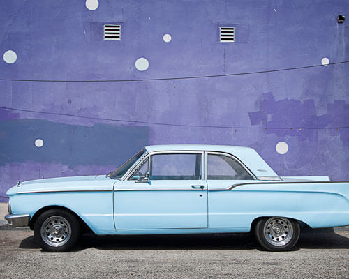 Blue car parked in front of a purple wall.