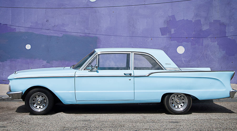 Blue car parked in front of a purple wall.