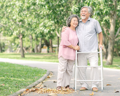 Couple smiling in the park with a walker.