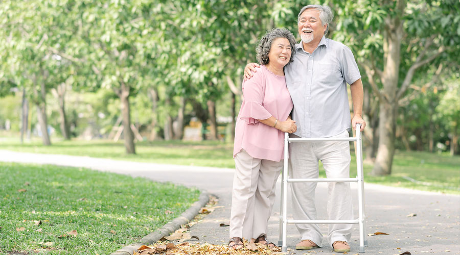 Couple smiling in a park with a walker.