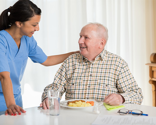Good Samaritan Society staff member talking with an elderly resident as he eats.