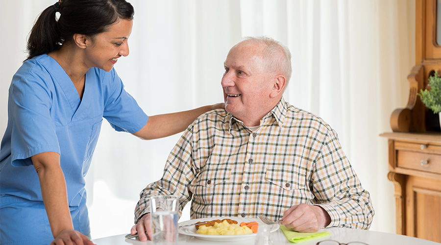 Good Samaritan Society staff member talking with an elderly resident as he eats.