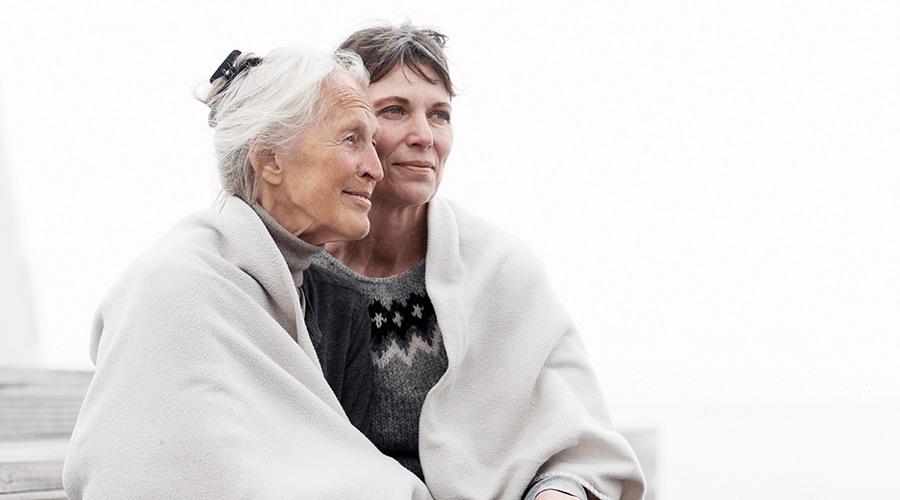 Mother and daughter snuggled close under a white blanket looking out.