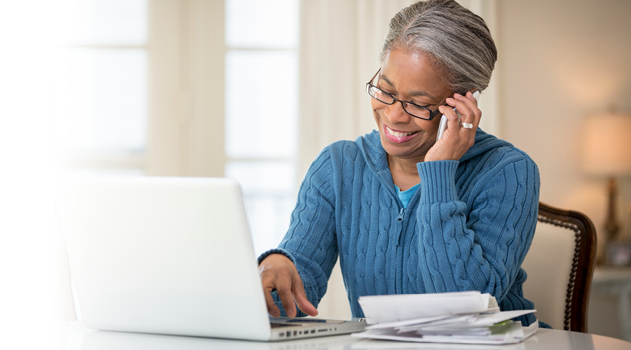 Older woman smiling while talking on the phone in front of her laptop.