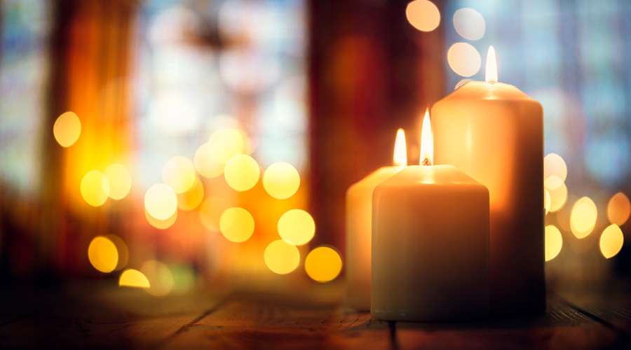 Three lit candles with decorative lights in the background
