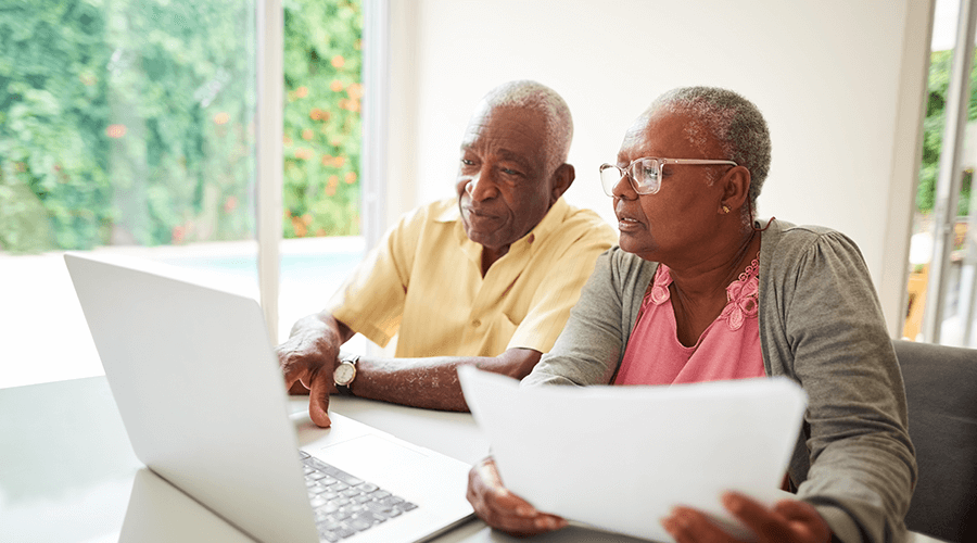 Older senior couple sitting together looking at a computer as go through advance care planning.
