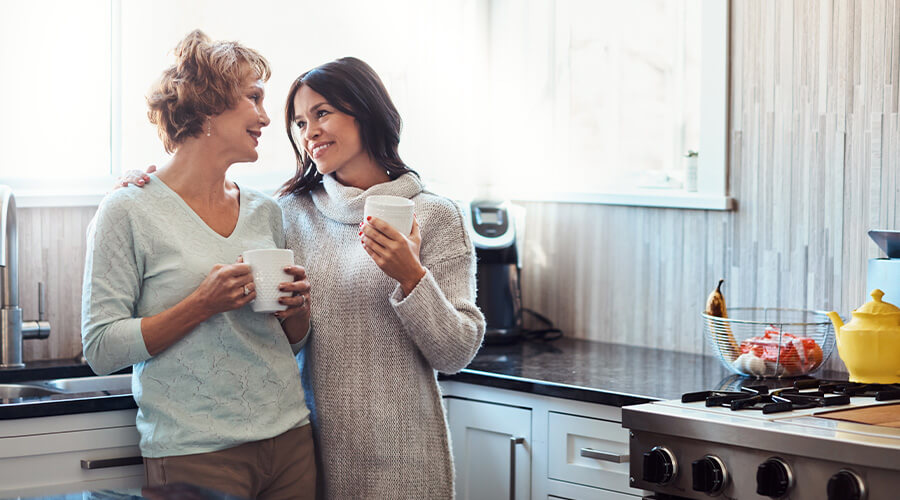 Older mother and daughter having a meaningful conversation while standing in the kitchen enjoying coffee.