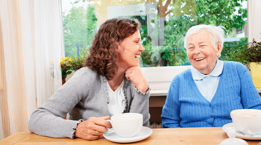 Mother and daughter laughing as they enjoy a cup of coffee at the kitchen table.