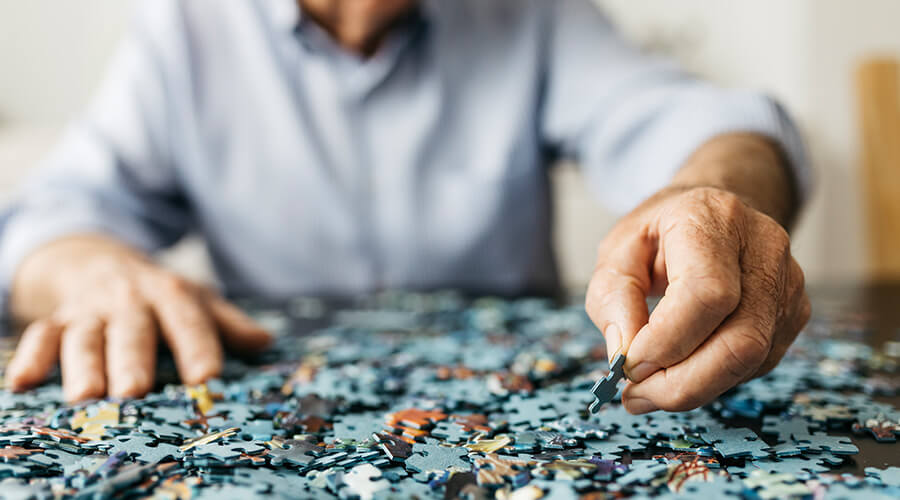 Elderly man, who lives in a nursing home, working on putting together a puzzle.