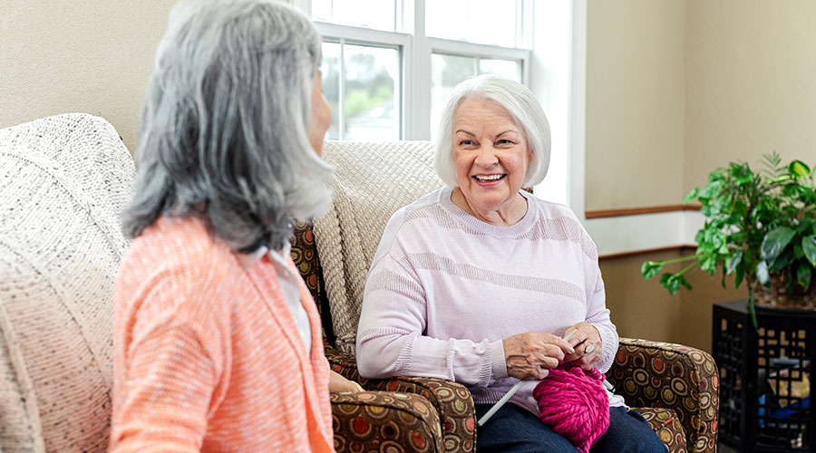 Two women sitting in chairs, knitting.