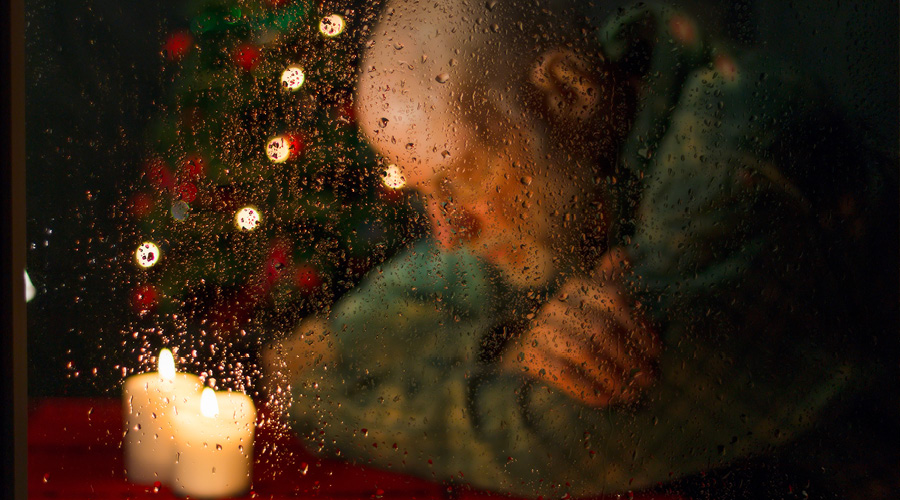 Older man with his arms crossed and his head down in front of a Christmas tree