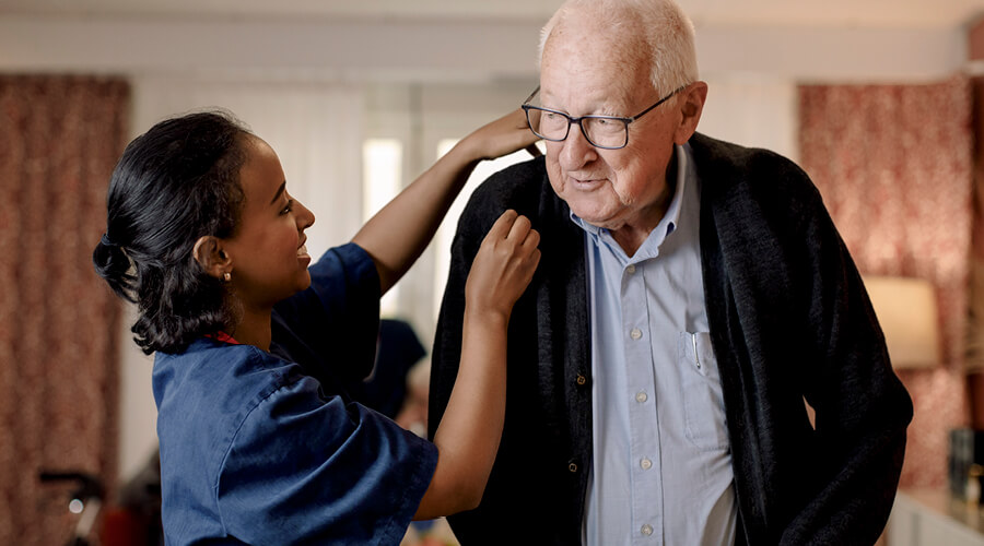 In-home nurse assisting senior gentleman with his jacket.
