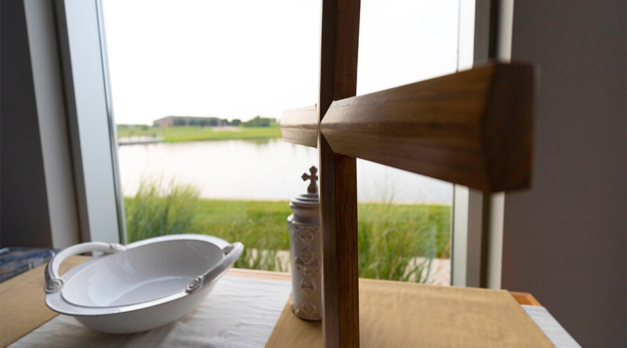 Wooden cross in front of a window facing a pond