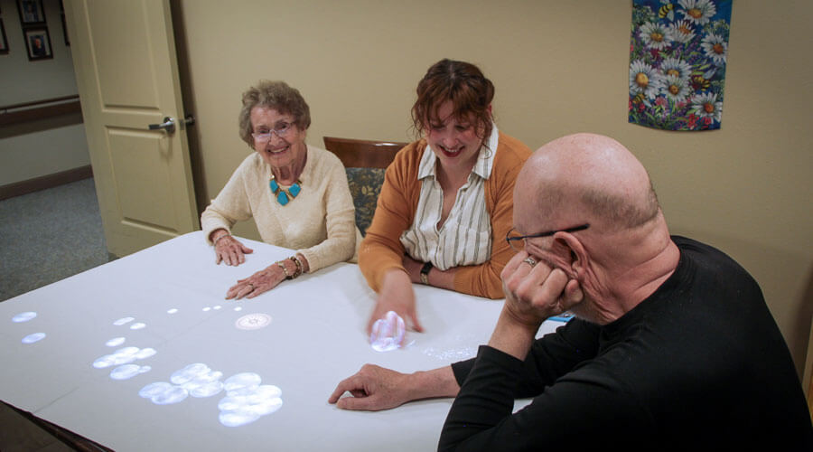 Memory care residents and staff pop bubbles being projected from the Tovertafel above the table.