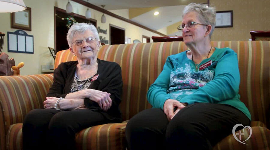 Carolyn Retzlaff and Diane Geis sit together on a couch.