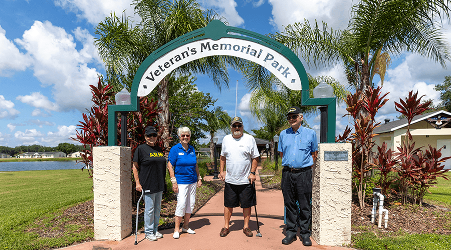 Four resident veterans standing in front of Veteran's Memorial Park at Kissimmee Village