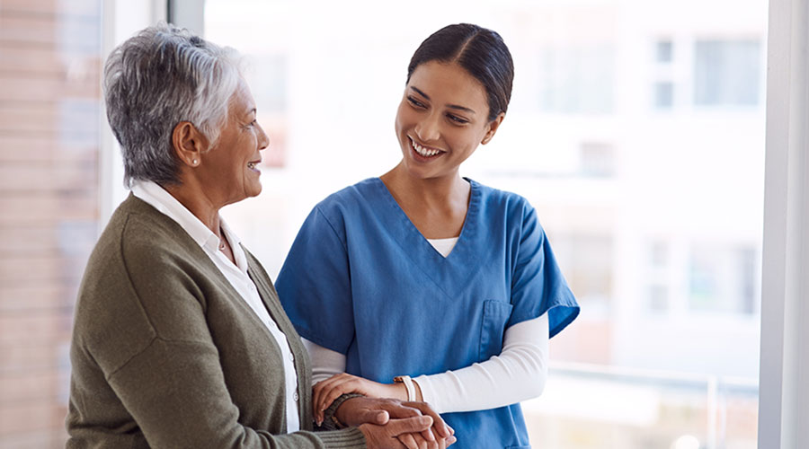 A young, ethnic, female nurse holding the hands of an older Black female